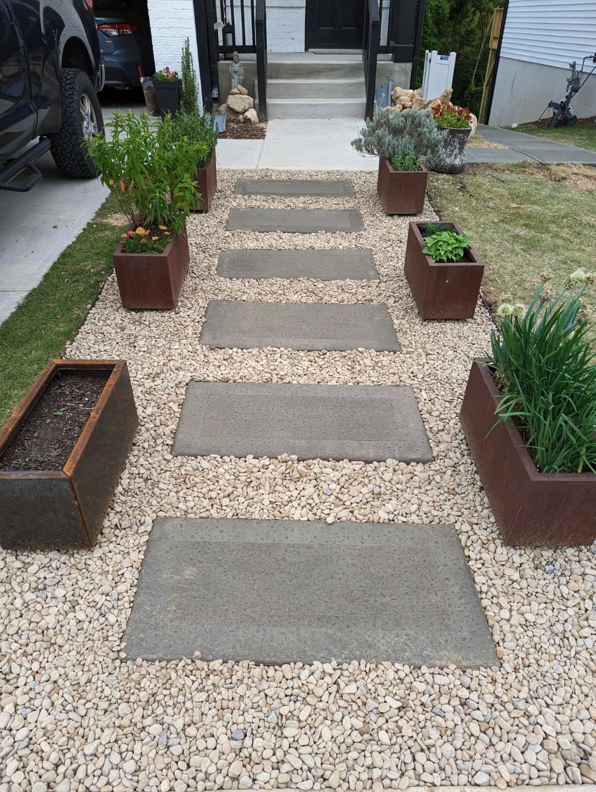 Concrete stepping pads set in gravel with planters along a front walk